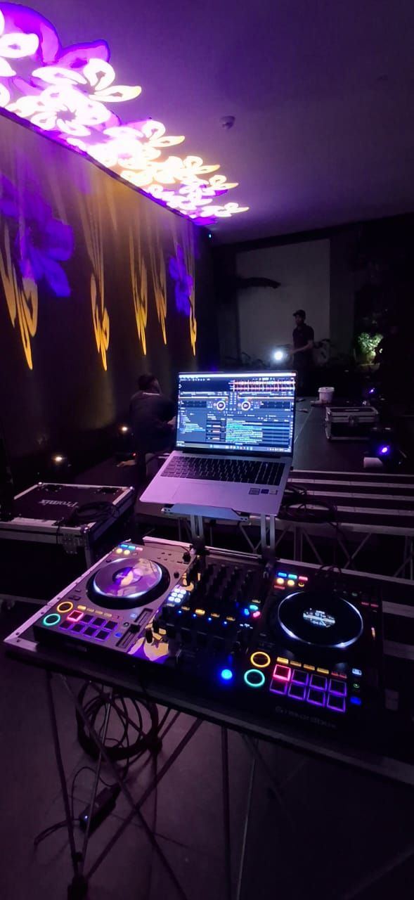 DJ controller and laptop on a stand in front of a wall lit with purple and gold floral gobo projections