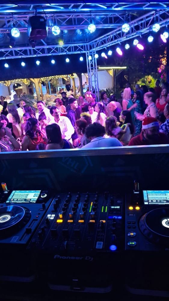 Crowded dancefloor at night under a truss lighting rig, seen from the DJ booth
