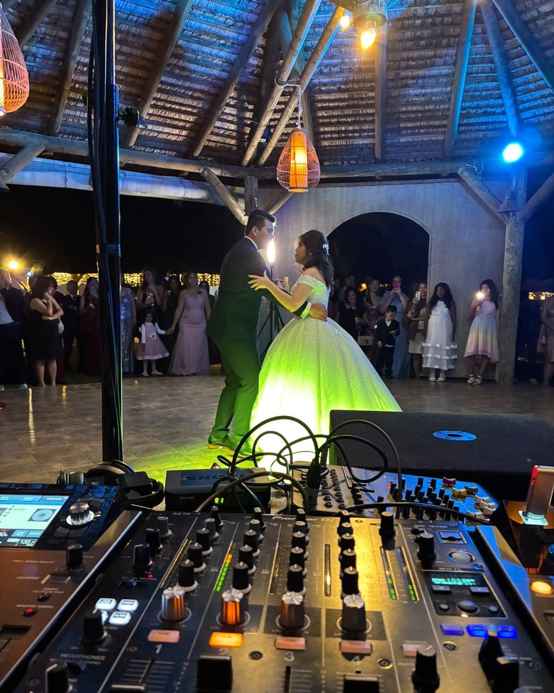 Bride and groom's first dance, DJ mixing desk in foreground, guests watching